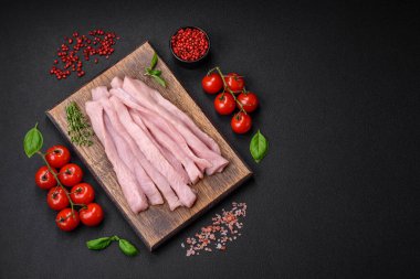 Çiğ tavuk ya da hindi filetosu koyu beton arka planda baharat ve otlarla şeritler halinde kesilmiş.