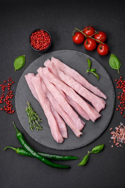 Çiğ tavuk ya da hindi filetosu koyu beton arka planda baharat ve otlarla şeritler halinde kesilmiş.