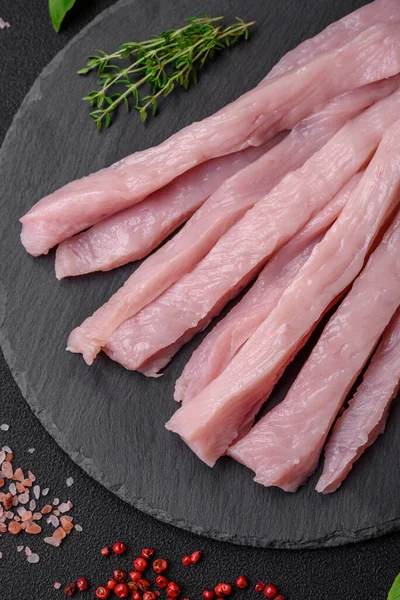 Çiğ tavuk ya da hindi filetosu koyu beton arka planda baharat ve otlarla şeritler halinde kesilmiş.