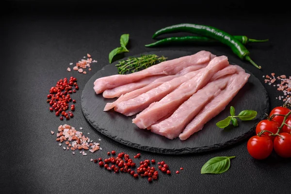 Çiğ tavuk ya da hindi filetosu koyu beton arka planda baharat ve otlarla şeritler halinde kesilmiş.