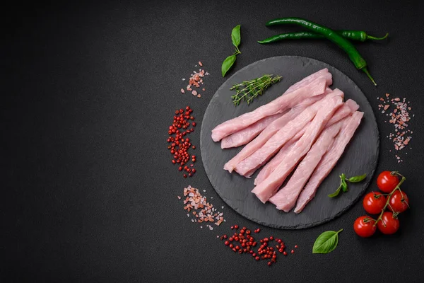 Çiğ tavuk ya da hindi filetosu koyu beton arka planda baharat ve otlarla şeritler halinde kesilmiş.