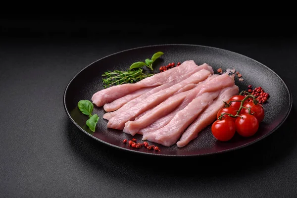 Çiğ tavuk ya da hindi filetosu koyu beton arka planda baharat ve otlarla şeritler halinde kesilmiş.