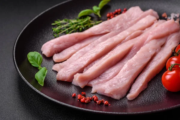 Çiğ tavuk ya da hindi filetosu koyu beton arka planda baharat ve otlarla şeritler halinde kesilmiş.