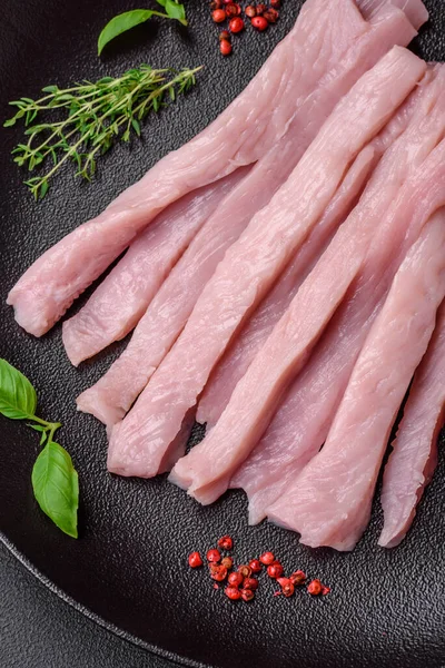 Çiğ tavuk ya da hindi filetosu koyu beton arka planda baharat ve otlarla şeritler halinde kesilmiş.