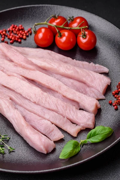 Çiğ tavuk ya da hindi filetosu koyu beton arka planda baharat ve otlarla şeritler halinde kesilmiş.