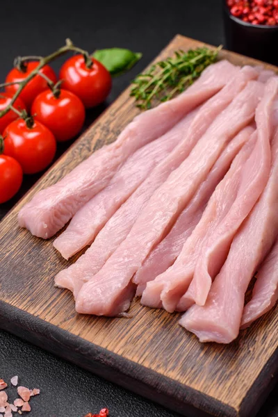 Çiğ tavuk ya da hindi filetosu koyu beton arka planda baharat ve otlarla şeritler halinde kesilmiş.