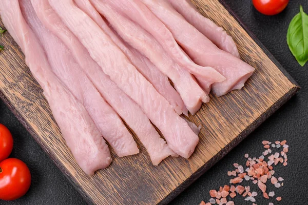 Çiğ tavuk ya da hindi filetosu koyu beton arka planda baharat ve otlarla şeritler halinde kesilmiş.