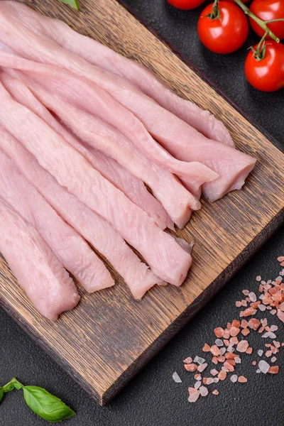 Çiğ tavuk ya da hindi filetosu koyu beton arka planda baharat ve otlarla şeritler halinde kesilmiş.