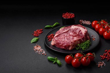 Taze, çiğ biftek, tuz, baharat ve otlar koyu dokulu arka planda.