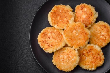 Kuru üzümlü ve vanilyalı lezzetli süzme peynirli kekler. Siyah seramik tabakta, koyu beton arka planda.