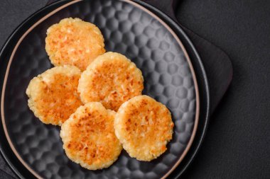 Kuru üzümlü ve vanilyalı lezzetli süzme peynirli kekler. Siyah seramik tabakta, koyu beton arka planda.