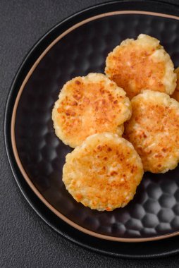 Kuru üzümlü ve vanilyalı lezzetli süzme peynirli kekler. Siyah seramik tabakta, koyu beton arka planda.