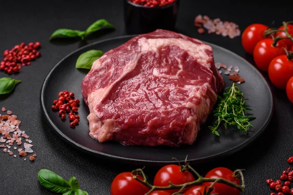 stock image Fresh, raw beef steak with salt, spices and herbs on a dark textured background