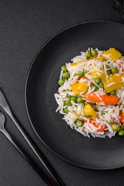 Lezzetli taze haşlanmış pirinç, sebzeli havuç, biber ve kuşkonmaz fasulyesi, koyu beton arka planda seramik bir tabakta.