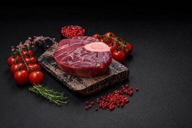 Fresh raw beef steak with bone or ossobuco with salt, spices and herbs on dark concrete background
