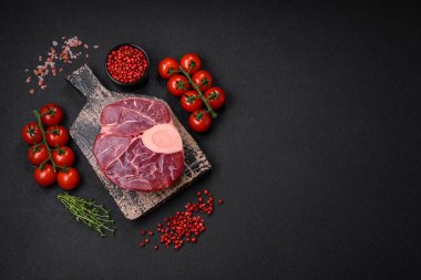 Fresh raw beef steak with bone or ossobuco with salt, spices and herbs on dark concrete background