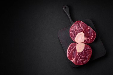 Fresh raw beef steak with bone or ossobuco with salt, spices and herbs on dark concrete background