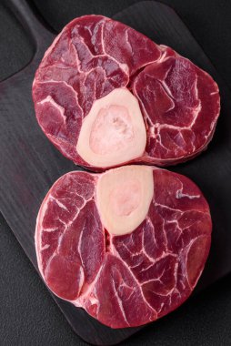 Fresh raw beef steak with bone or ossobuco with salt, spices and herbs on dark concrete background