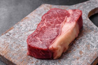 Taze çiğ biftek, tuz, baharat ve otlarla birlikte koyu beton bir arka planda.