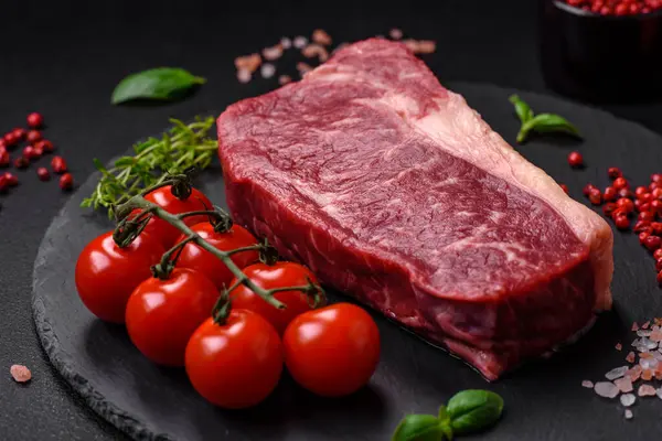 stock image Fresh raw beef striploin steak with salt, spices and herbs on a dark concrete background