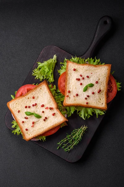 夹杂着烤面包 西红柿 奶酪和生菜 香料和香草的美味三明治 背景为深色混凝土 — 图库照片