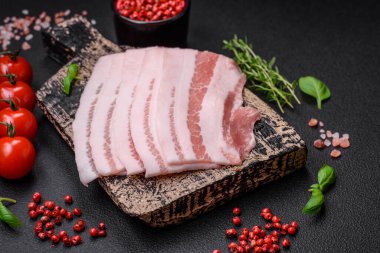 Taze çiğ pastırma, tuz, baharat ve otlarla dilimlenmiş koyu dokulu beton arka planda.