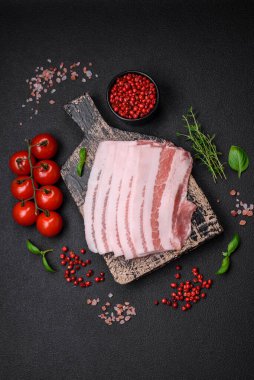 Taze çiğ pastırma, tuz, baharat ve otlarla dilimlenmiş koyu dokulu beton arka planda.