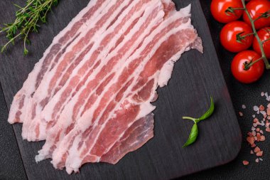 Taze çiğ pastırma, tuz, baharat ve otlarla dilimlenmiş koyu dokulu beton arka planda.