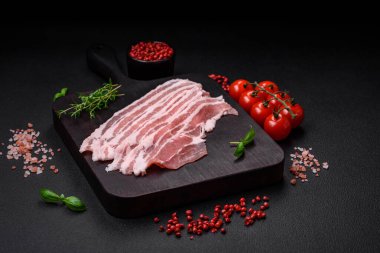 Taze çiğ pastırma, tuz, baharat ve otlarla dilimlenmiş koyu dokulu beton arka planda.