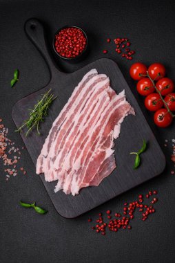 Taze çiğ pastırma, tuz, baharat ve otlarla dilimlenmiş koyu dokulu beton arka planda.