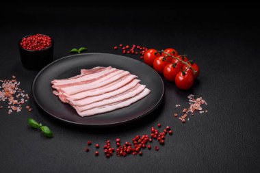 Taze çiğ pastırma, tuz, baharat ve otlarla dilimlenmiş koyu dokulu beton arka planda.