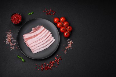 Taze çiğ pastırma, tuz, baharat ve otlarla dilimlenmiş koyu dokulu beton arka planda.