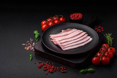 Taze çiğ pastırma, tuz, baharat ve otlarla dilimlenmiş koyu dokulu beton arka planda.