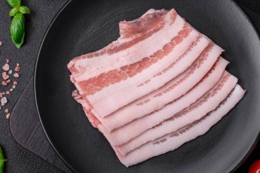 Taze çiğ pastırma, tuz, baharat ve otlarla dilimlenmiş koyu dokulu beton arka planda.