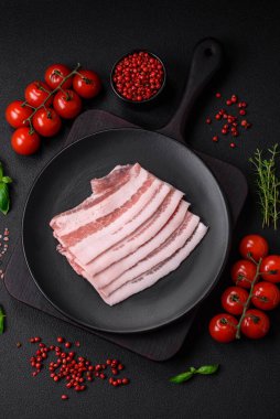 Taze çiğ pastırma, tuz, baharat ve otlarla dilimlenmiş koyu dokulu beton arka planda.