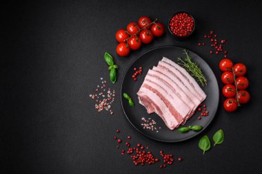 Taze çiğ pastırma, tuz, baharat ve otlarla dilimlenmiş koyu dokulu beton arka planda.