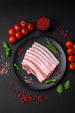 Taze çiğ pastırma, tuz, baharat ve otlarla dilimlenmiş koyu dokulu beton arka planda.