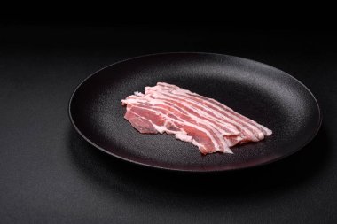 Taze çiğ pastırma, tuz, baharat ve otlarla dilimlenmiş koyu dokulu beton arka planda.