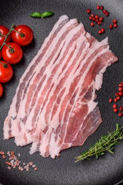 Taze çiğ pastırma, tuz, baharat ve otlarla dilimlenmiş koyu dokulu beton arka planda.
