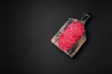 Lezzetli tütsülenmiş salam sosisi, tuz, baharat ve otlar koyu beton arka planda dilimler halinde kesilmiş.