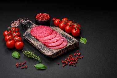 Lezzetli tütsülenmiş salam sosisi, tuz, baharat ve otlar koyu beton arka planda dilimler halinde kesilmiş.