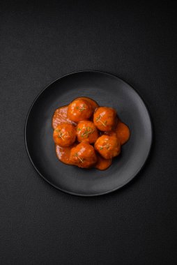 Lezzetli taze köfteler, tuz, baharat ve çimento arkaplanda bitkilerle birlikte domates sosu.