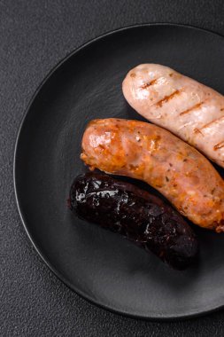 Tuz, baharat ve otlarla ızgara yapılmış lezzetli, sulu sosisler koyu beton bir arka planda.