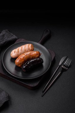 Tuz, baharat ve otlarla ızgara yapılmış lezzetli, sulu sosisler koyu beton bir arka planda.