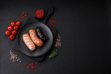 Tuz, baharat ve otlarla ızgara yapılmış lezzetli, sulu sosisler koyu beton bir arka planda.