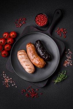 Tuz, baharat ve otlarla ızgara yapılmış lezzetli, sulu sosisler koyu beton bir arka planda.
