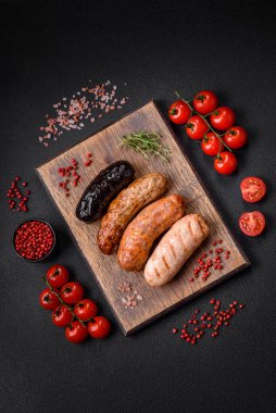 Tuz, baharat ve otlarla ızgara yapılmış lezzetli, sulu sosisler koyu beton bir arka planda.