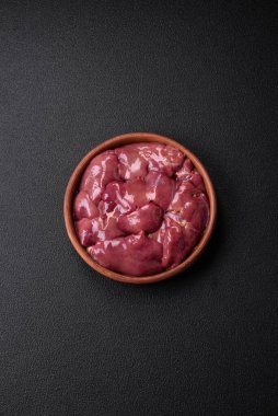 Taze çiğ tavuk veya seramik tabakta hindi ciğeri. Koyu beton arka planda tuz, baharat ve otlarla birlikte.