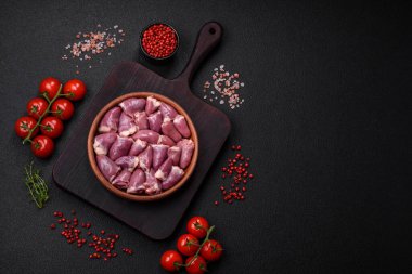 Taze çiğ tavuk ya da seramik tabakta hindi kalbi. Koyu beton arka planda tuz, baharat ve otlarla birlikte.