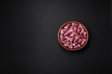 Taze çiğ tavuk ya da seramik tabakta hindi kalbi. Koyu beton arka planda tuz, baharat ve otlarla birlikte.